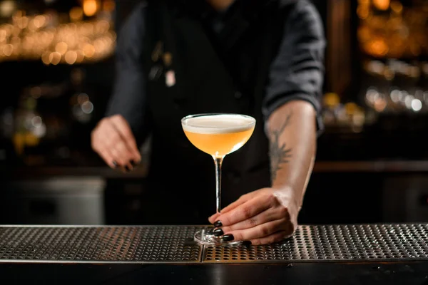 Getatoeëerde barkeeper meisje serveert de gele alcoholische cocktail drank met een wit uitschot — Stockfoto