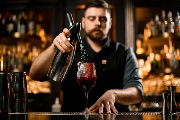 Mannelijke barman schenkt een drankje van de sifon in een glas met ijs en rood kruid decor — Stockfoto