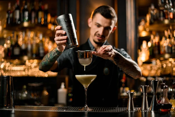 Professionele barman gieten gele romige alcoholische drank uit de shaker naar het glas door de zeef filter — Stockfoto