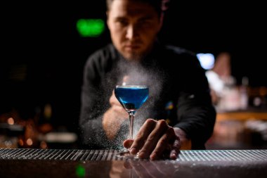 Bartender spraying on the blue alcoholic drink with a bitter to serve it clipart