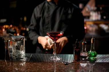 Profesyonel erkek barmen, uzun bardakta buz küpleriyle kırmızı alkollü kokteyl servis ediyor.