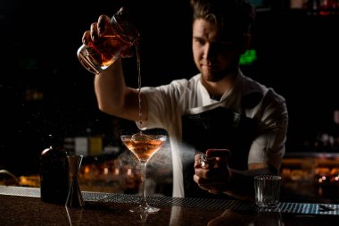 Kahverengi alkollü içeceğe sprey sıkan profesyonel barmen bardağa acı döküyor.