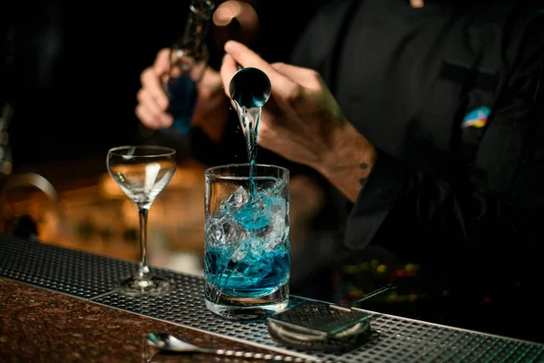 Barman professionnel versant une boisson alcoolisée bleue du jigger à une tasse à mesurer tenant une bouteille en verre — Photo