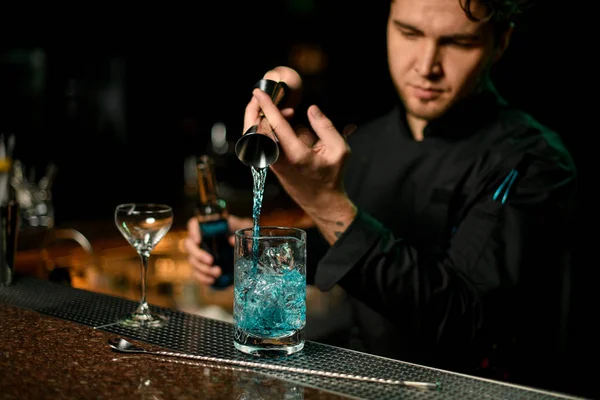 Cantinero profesional sirviendo una bebida alcohólica azul del jigger a una taza de medir — Foto de Stock