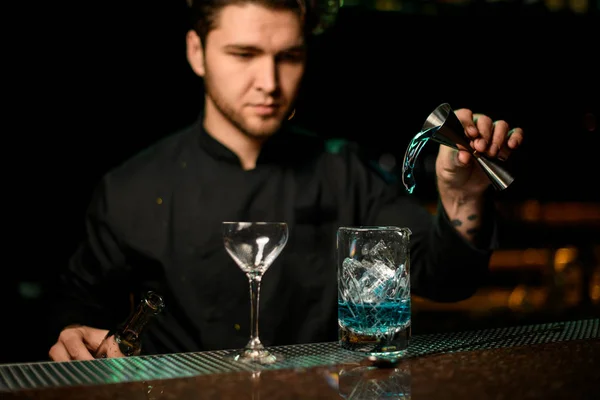 Професійний чоловічий бармен, що поливає синій алкогольний напій від джига до мірної чашки — стокове фото