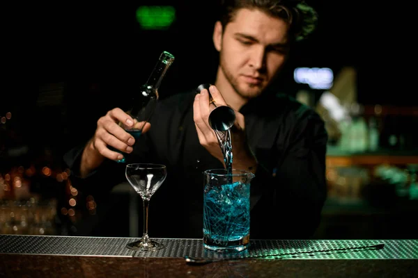 Професійний бармен, що поливає синій алкогольний лікер від цигарки до мірної чашки — стокове фото