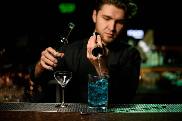 Професійний чоловічий бармен наливає блакитний алкогольний лікер з джига до мірної чашки — стокове фото