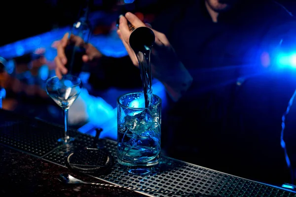 Cantinero profesional que vierte un licor alcohólico azul del jigger a una taza medidora bajo luz azul —  Fotos de Stock