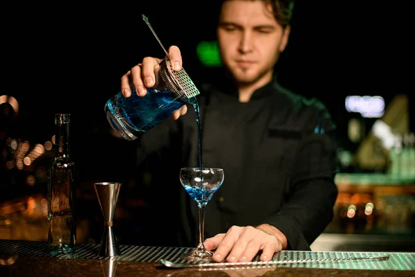 Cantinero masculino profesional que vierte una bebida alcohólica de la taza de medir al vaso a través del filtro colador —  Fotos de Stock