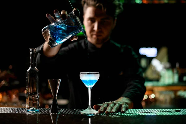 Cantinero masculino profesional que vierte una bebida alcohólica azul de la taza de medir al vaso a través del filtro colador —  Fotos de Stock
