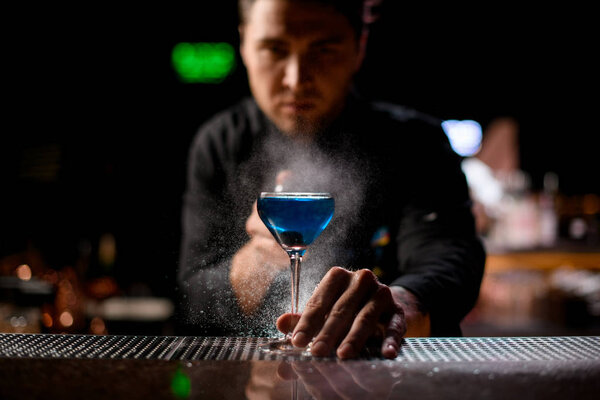 Bartender spraying on the blue alcoholic drink with a bitter to serve it
