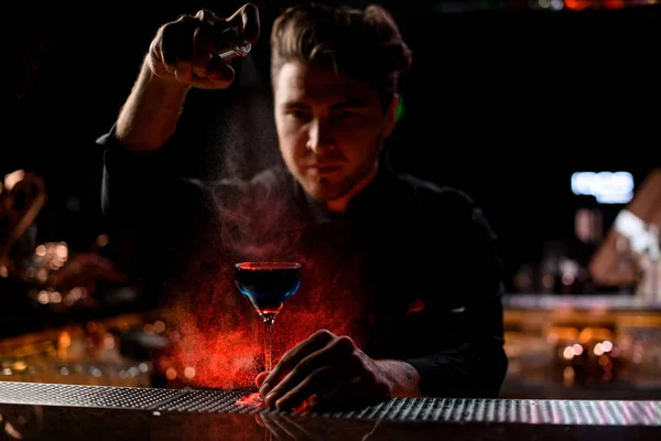 Професійний чоловічий бармен розбризкує синій алкогольний коктейль з гірким під червоним світлом — стокове фото