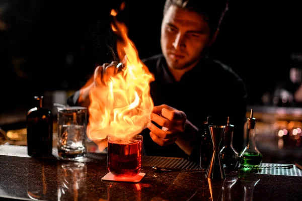 Cantinero sirviendo el cóctel alcohólico rojo con cubitos de hielo bajo el fuego —  Fotos de Stock