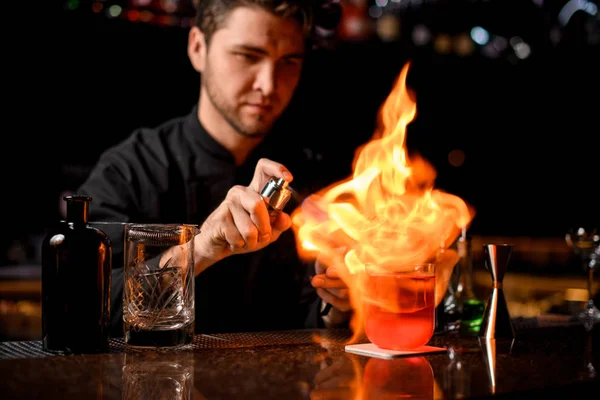 Cantinero macho sirviendo el cóctel alcohólico rojo con hielo bajo el fuego —  Fotos de Stock
