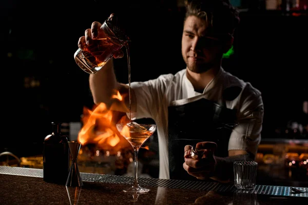 Профессиональный бармен разливает коричневый алкогольный коктейль от мерной чашки до стекла в огонь — стоковое фото