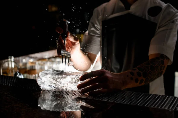 Profesyonel erkek barmen büyük bir buz parçasını özel bir aletle kazıklıyor. — Stok fotoğraf