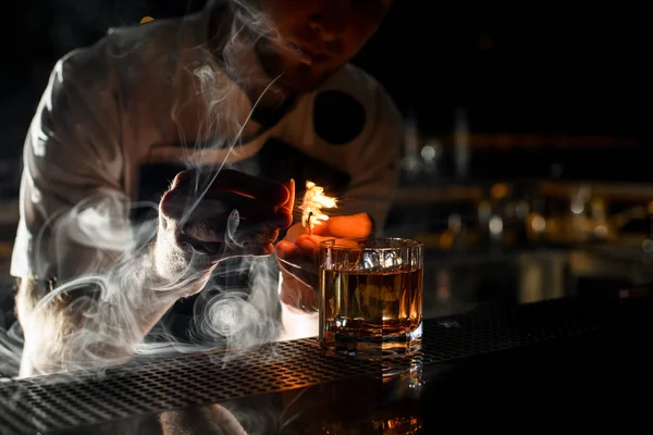 Barista professionista di sesso maschile che serve il cocktail alcolico trasparente cosparso con il succo di limone sul fiammifero facendo fuoco — Foto Stock