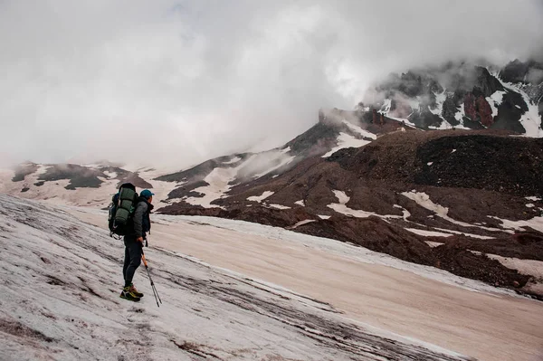 Tourist mit Rucksack und Stöcken blickt auf Berg — Stockfoto