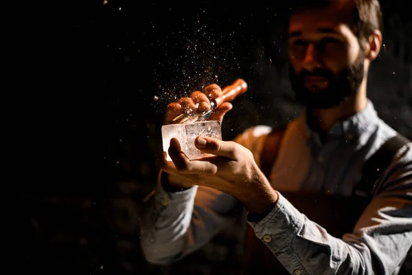 Professionell manlig bartender med skägg skära is med en speciell gaffel i baren i mörkret — Stockfoto