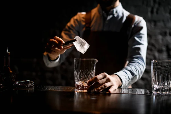 Profesjonalny mężczyzna barman wprowadzenie kostki lodu z pincety do szkła — Zdjęcie stockowe