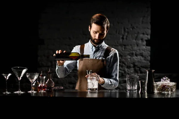 Мужчина-бармен с бородой, наливающий алкогольный напиток из бутылки в стальной контейнер — стоковое фото