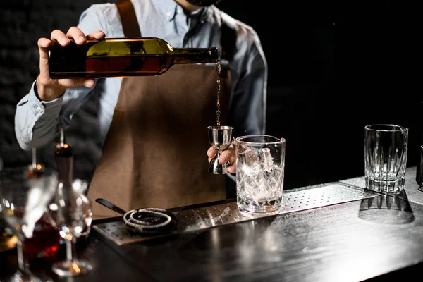 Cantinero macho sirviendo una bebida alcohólica de la botella a un jigger de acero —  Fotos de Stock