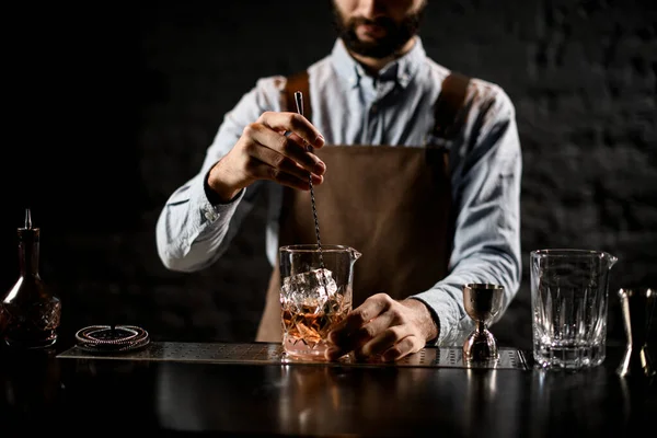 Erkek barmen, özel kaşıkla bardakta buz olan kahverengi bir kokteyli karıştırıyor. — Stok fotoğraf