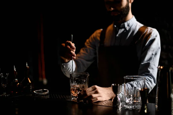 Male bartender stirring a golden cocktail with ice cubes in the glass with special spoon — Stock Photo, Image