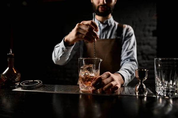 Professionell bartender som rör om i en gyllene cocktail med isbitar i glaset med specialsked — Stockfoto