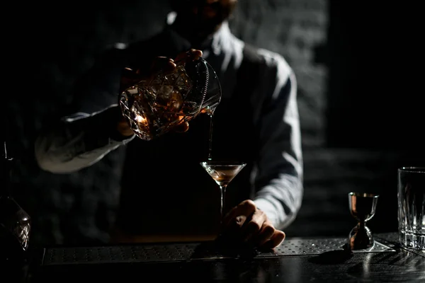 Профессиональный бармен наливает золотой алкогольный напиток из мерного стакана со странником в бокал мартини — стоковое фото