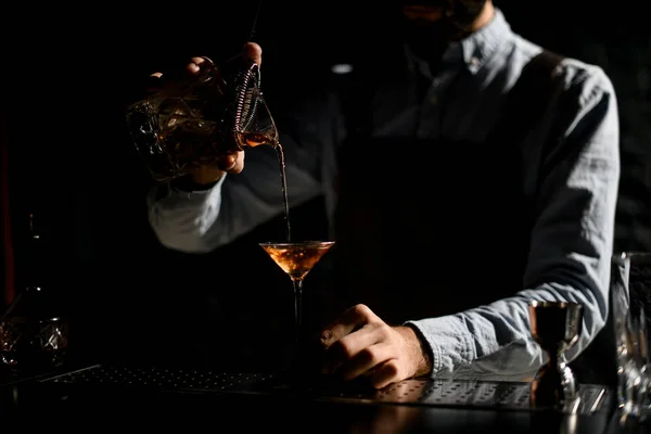 Barista professionista che versa una bevanda alcolica dorata dal misurino con straner a un bicchiere da martini — Foto Stock