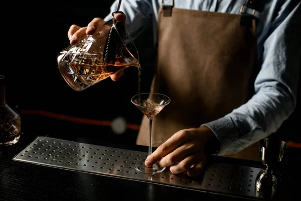 Barista maschio versando una bevanda alcolica marrone dal misurino con straner a un bicchiere da martini — Foto Stock
