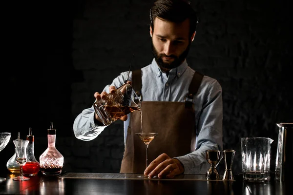 Barista versando una bevanda alcolica d'oro dal misurino con straner ad un bicchiere da martini — Foto Stock