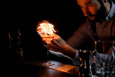 Çekici erkek barmen, martini bardağında altın alkollü içeceğe orage lezzeti ile çakmak spreyliyor.