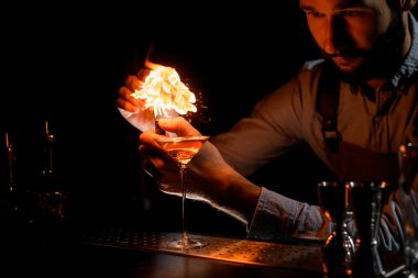 Barmen çakmağa martini bardağında altın alkollü içeceğe meyve suyu sıkıyor.