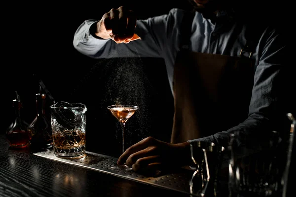 Csapos lepermetez egy barna alkoholos italt egy martinis pohárban, narancslével. — Stock Fotó