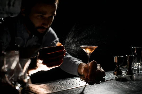 Cantinero rociando una bebida alcohólica dorada en un vaso de martini con jugo de ralladura de orage —  Fotos de Stock