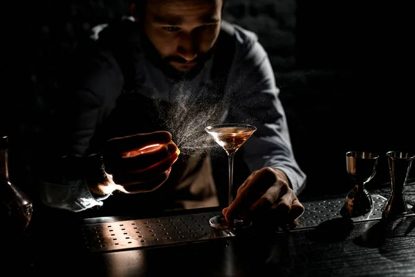 Cantinero profesional rociando la bebida alcohólica de oro en un vaso de martini con jugo de ralladura de orage —  Fotos de Stock