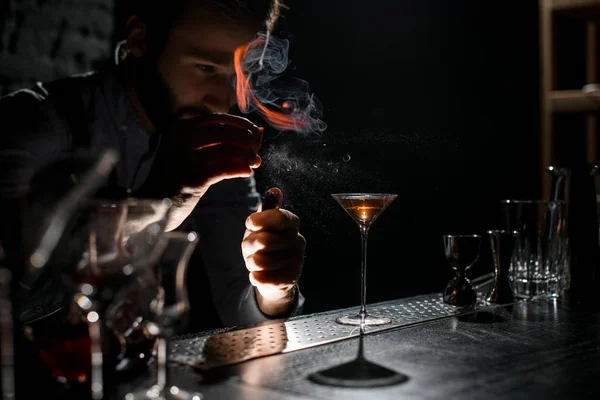 Barista maschio professionale che spruzza su un accendino con succo di scorza di orage alla bevanda alcolica d'oro in un bicchiere da martini — Foto Stock