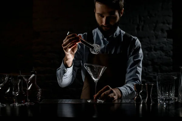 Профессиональный бармен кладет кубик льда с твизерами в высокий бокал мартини — стоковое фото