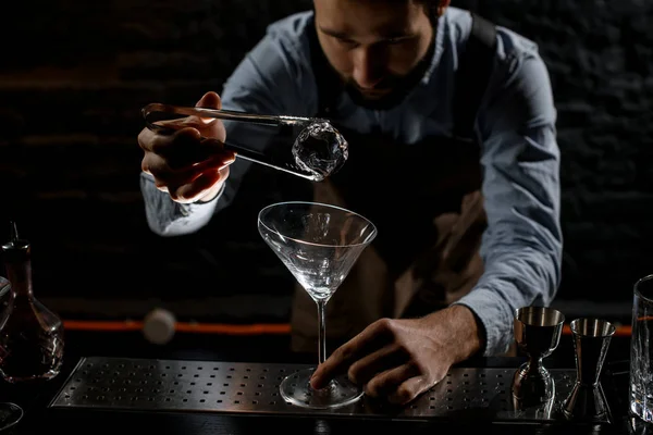 Barista professionista mettendo cubetto di ghiaccio con twezzers al bicchiere Martini alto — Foto Stock