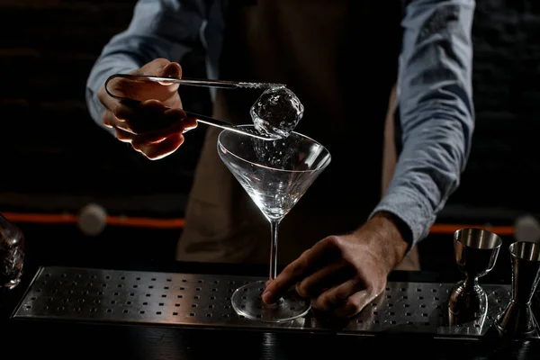 Mężczyzna barman wprowadzenie kostka lodu z twezzers dla wysoki martini szklanka — Zdjęcie stockowe