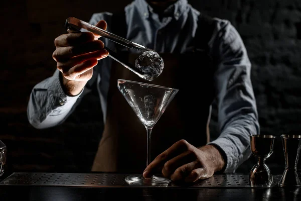 Cantinero poniendo cubo de hielo con pinzas para el vaso de martini alto — Foto de Stock