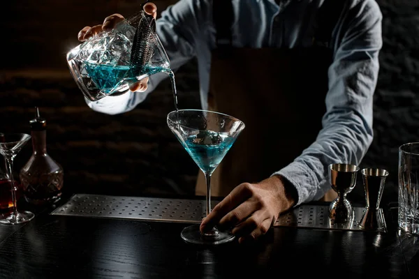 Cantinero macho que vierte una bebida alcohólica azul de la taza de medir con colador a una copa de martini — Foto de Stock