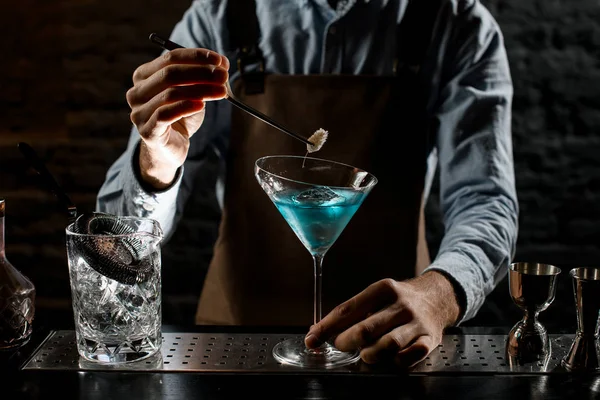 Мужчина-бармен деакорит синий алкогольный коктейль в бокале мартини с шипом — стоковое фото