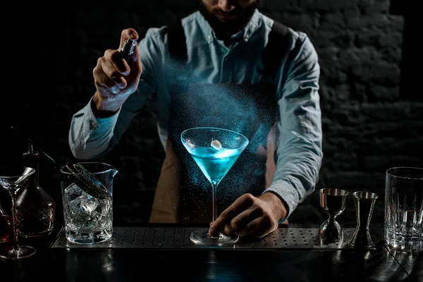 Επαγγελματίας μπάρμαν ψεκάζει με ένα πικρό σε ένα μπλε αλκοολούχο κοκτέιλ σε ένα ποτήρι μαρτίνι διακοσμημένο με μια πινέζα — Φωτογραφία Αρχείου