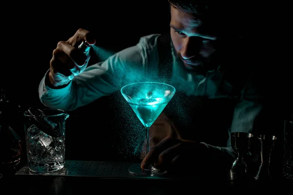 Бармен брызгает горьким на синий алкогольный коктейль в бокале мартини, украшенном шипом — стоковое фото