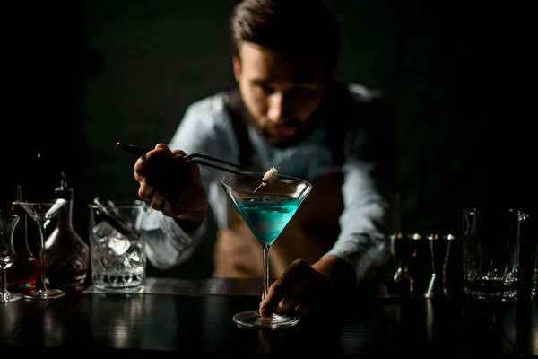 Barista professionista che disacora un cocktail alcolico blu in un bicchiere da martini con una spikelet con twezzers — Foto Stock