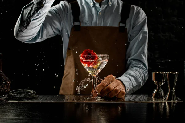 Cantinero macho lanzando un gran capullo de rosa roja a una copa de martini con un cóctel alcohólico — Foto de Stock