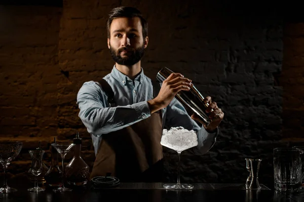 Cantinero profesional con una barba sosteniendo un agitador de acero en el mostrador de la barra con el equipo de la barra —  Fotos de Stock